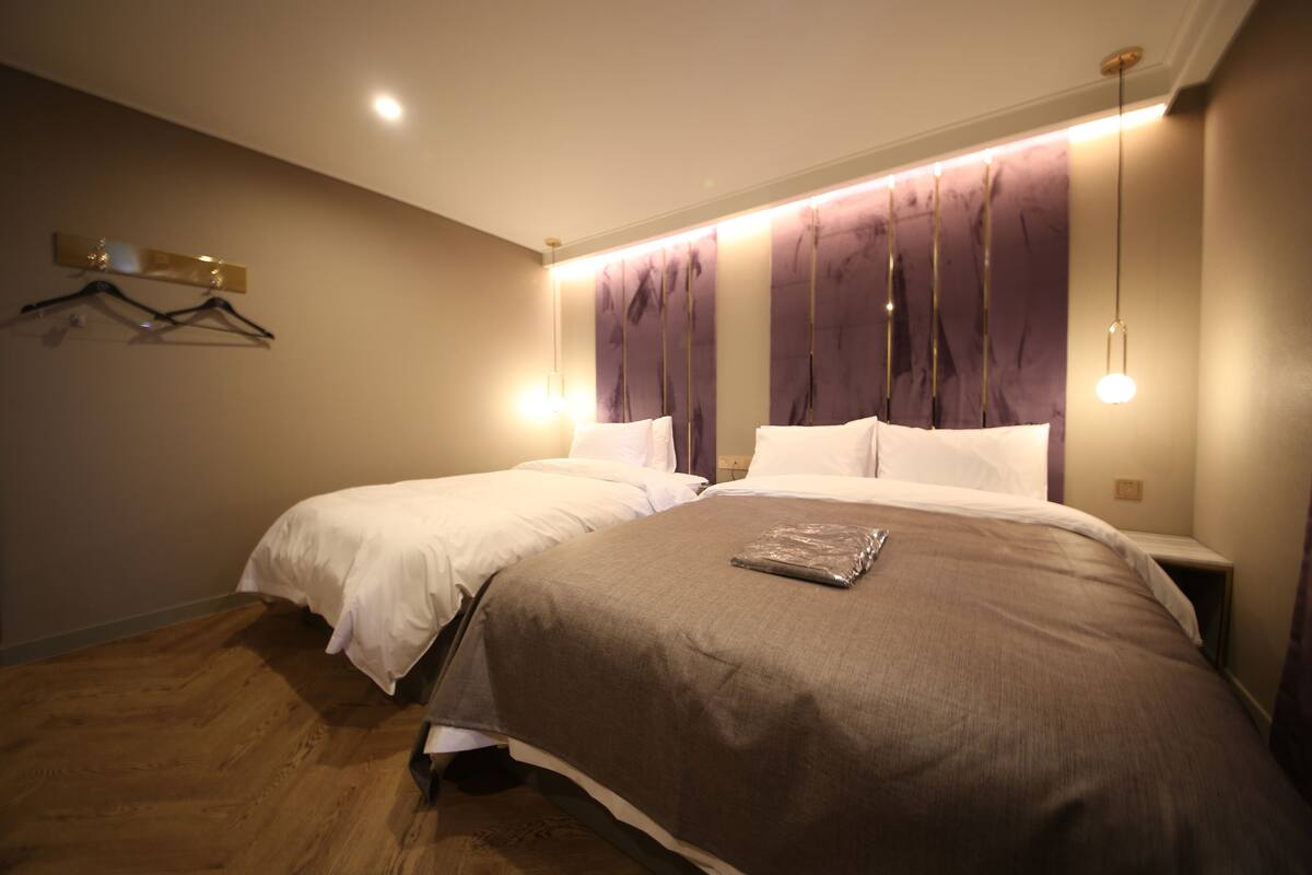 Habitación de hotel con dos camas, suelo de madera y una lámpara de pared.