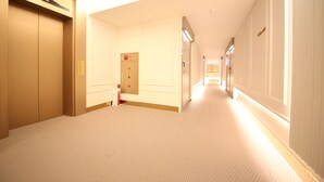 Ein Hotelkorridor mit Teppichboden, einer Tür mit rotem Notrufknopf und einer Leuchte an der Decke.
