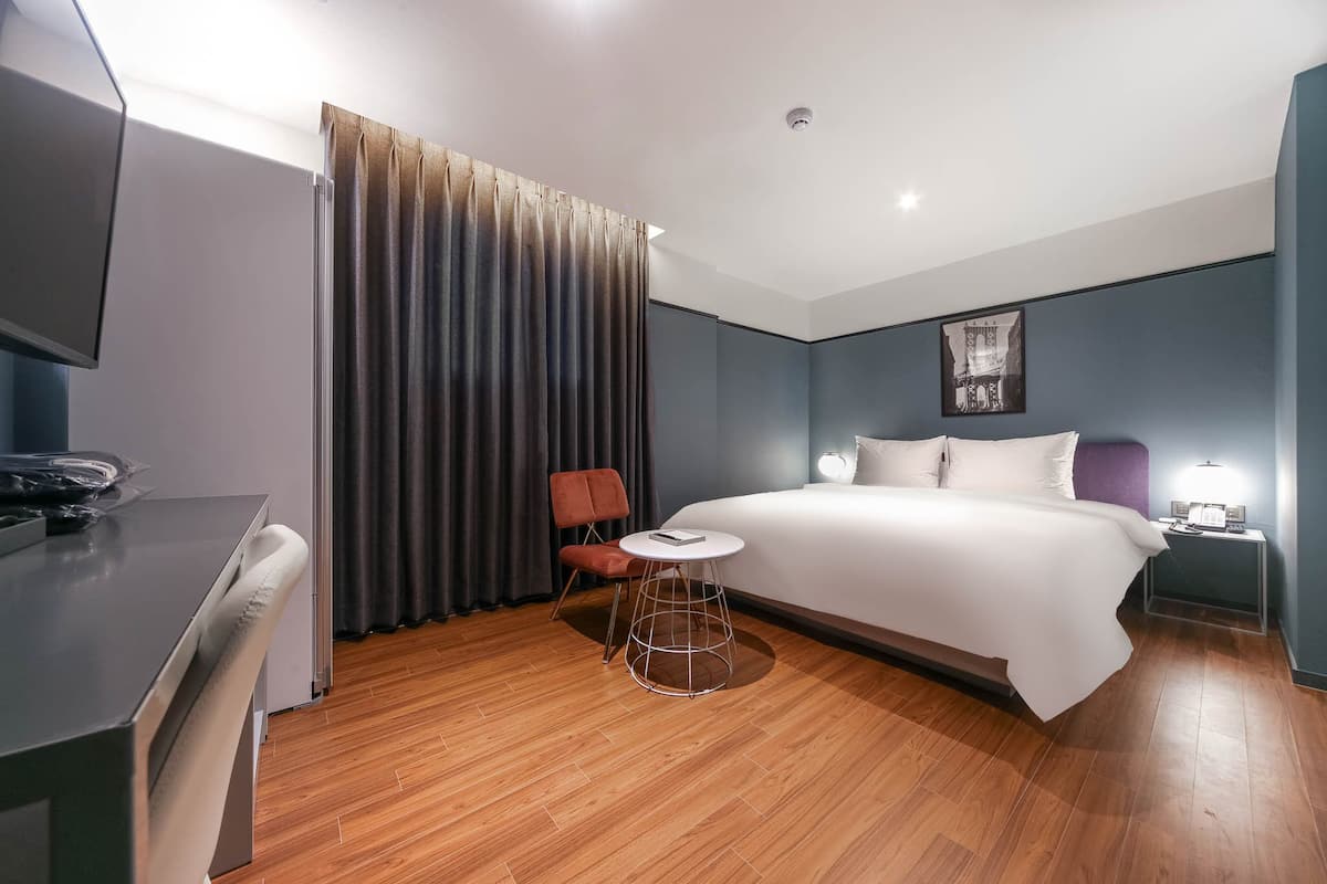 Ein Hotelzimmer mit Bett, Schreibtisch, Stuhl, kleinem Tisch und Vorhang.