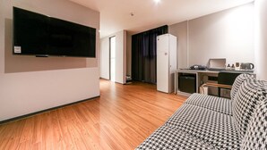 A modern living room with a flat-screen TV, a houndstooth sofa, a kitchen area with a refrigerator, and a wooden floor. - Pohang Brown Dot Hotel (Pohang)