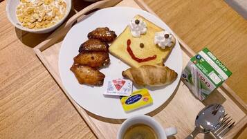 Bandeja de desayuno con cereal, bolitas de chocolate, pollo frito, un croissant, una cara sonriente hecha con comida, una cajita de mantequilla, una taza de café y una cuchara.