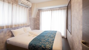 Habitación de hotel con cama, aire acondicionado y ventanas grandes con cortinas.