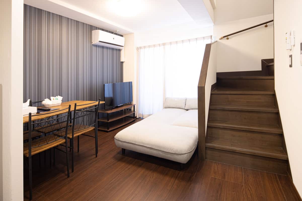 Kompakti hotellihuone, jossa on puulattia, pieni työpöytä tuolilla, sänky ja portaikko.