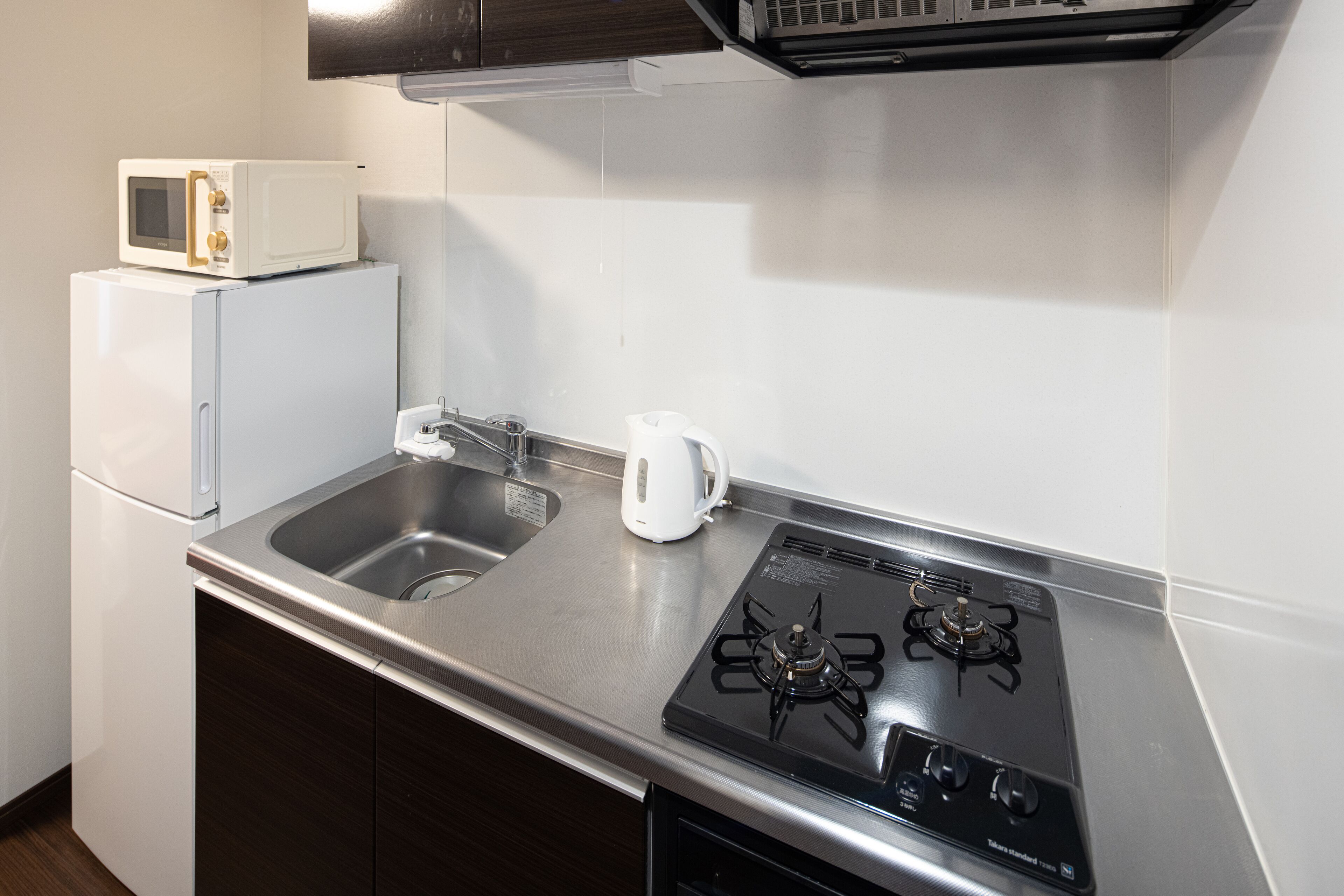 Une cuisine compacte équipée d’un four à micro-ondes encastré, d’une machine à café et d’une cuisinière à gaz.