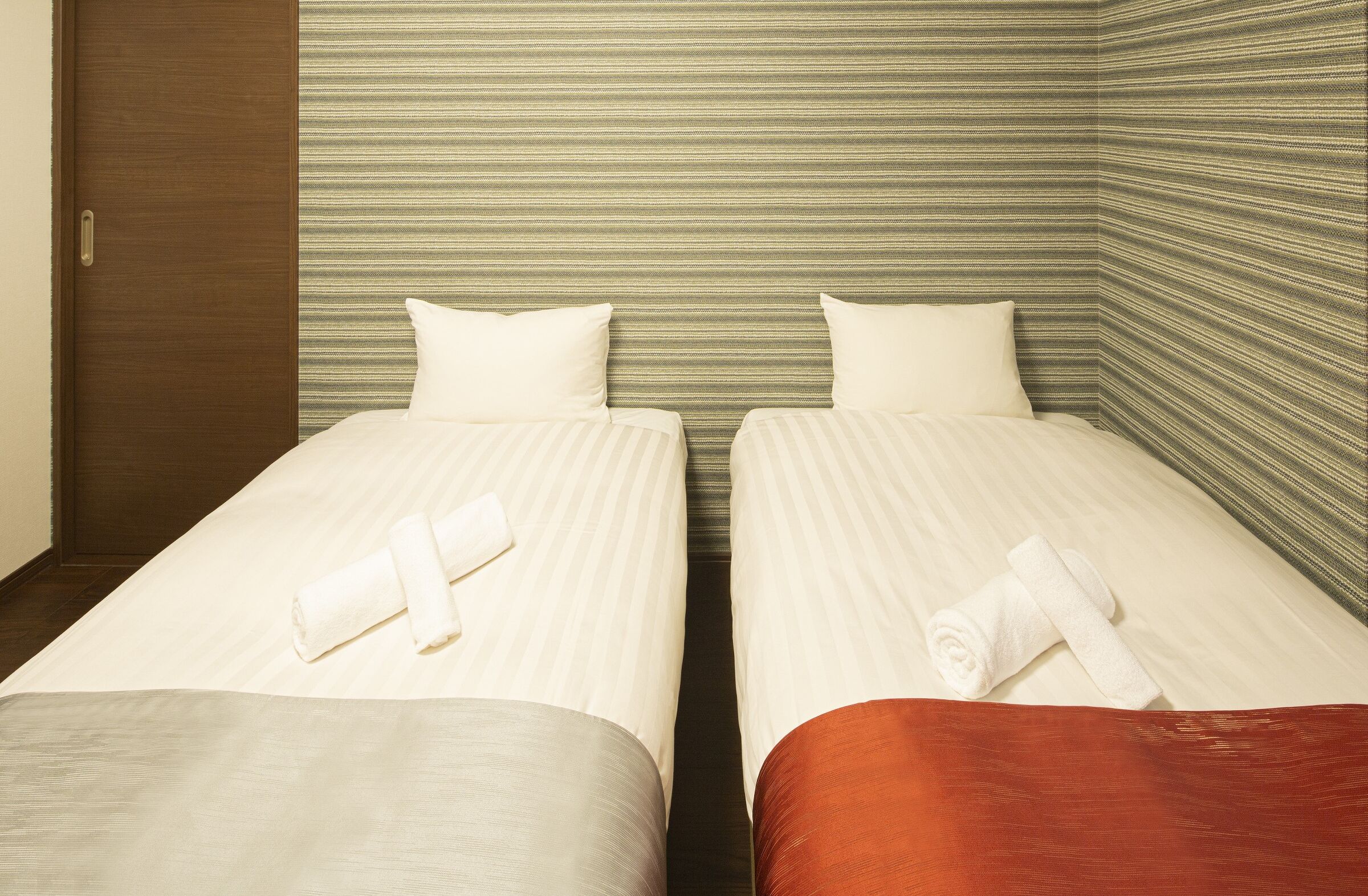 Habitación de hotel con dos camas individuales, cada una con una almohada y una toalla enrollada.