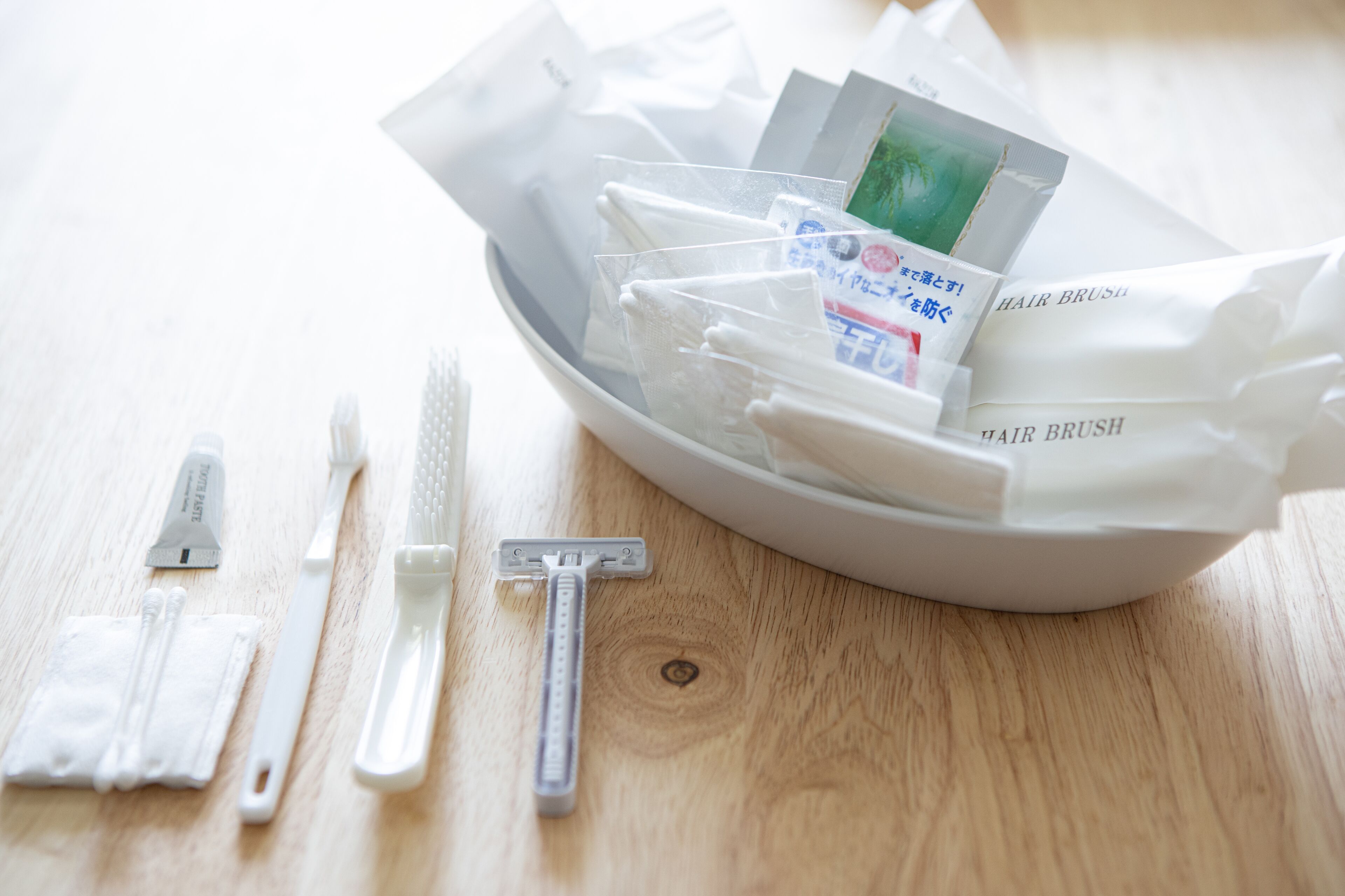 Eine weiße Schale mit verschiedenen Pflegeutensilien wie Rasierern, einer Bürste und einer Zahnbürste auf einer Holztischplatte.