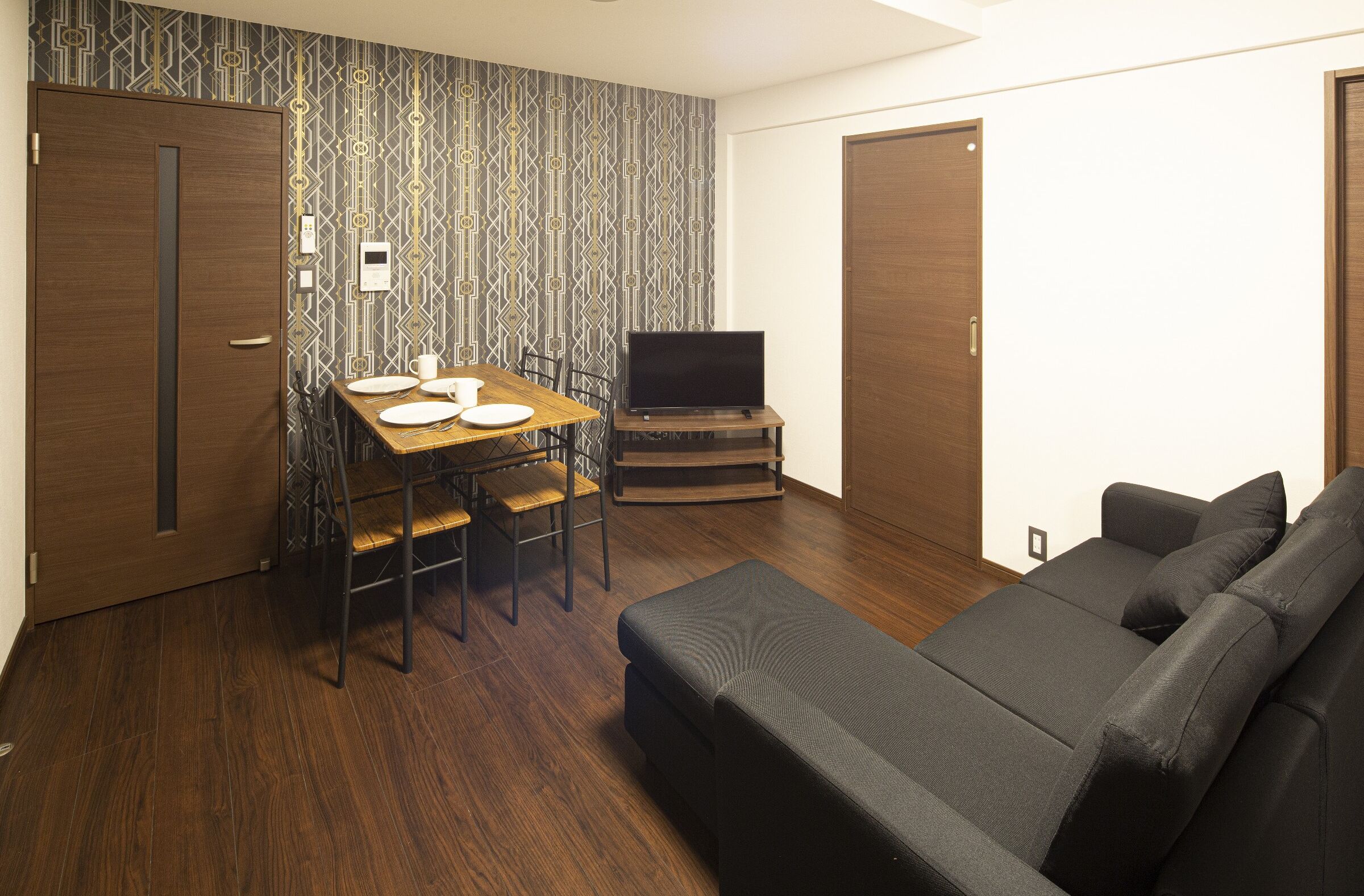A compact living space with a wooden floor, a sofa, a dining table with chairs, and a television on a stand.