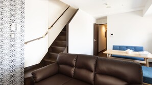 Una sala de estar moderna con un sofá de cuero marrón, una mesa de centro de madera y un sofá azul al fondo.
