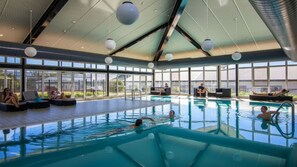 En inomhuspool med fri utsikt mot omgivningen, stora fönster och en modern takdesign.