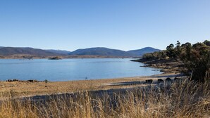 A lake with a clear view of distant mountains, a sandy shoreline, and dry grass in the foreground.
