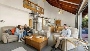 A spacious living room with a high ceiling, a staircase, and a kitchen in the background.
