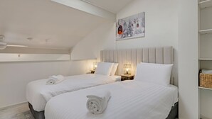 A hotel room with two beds, a ceiling fan, a painting, and a shelf with baskets. - Razorback 15 - Central Jindabyne CBD Unit (Jindabyne)