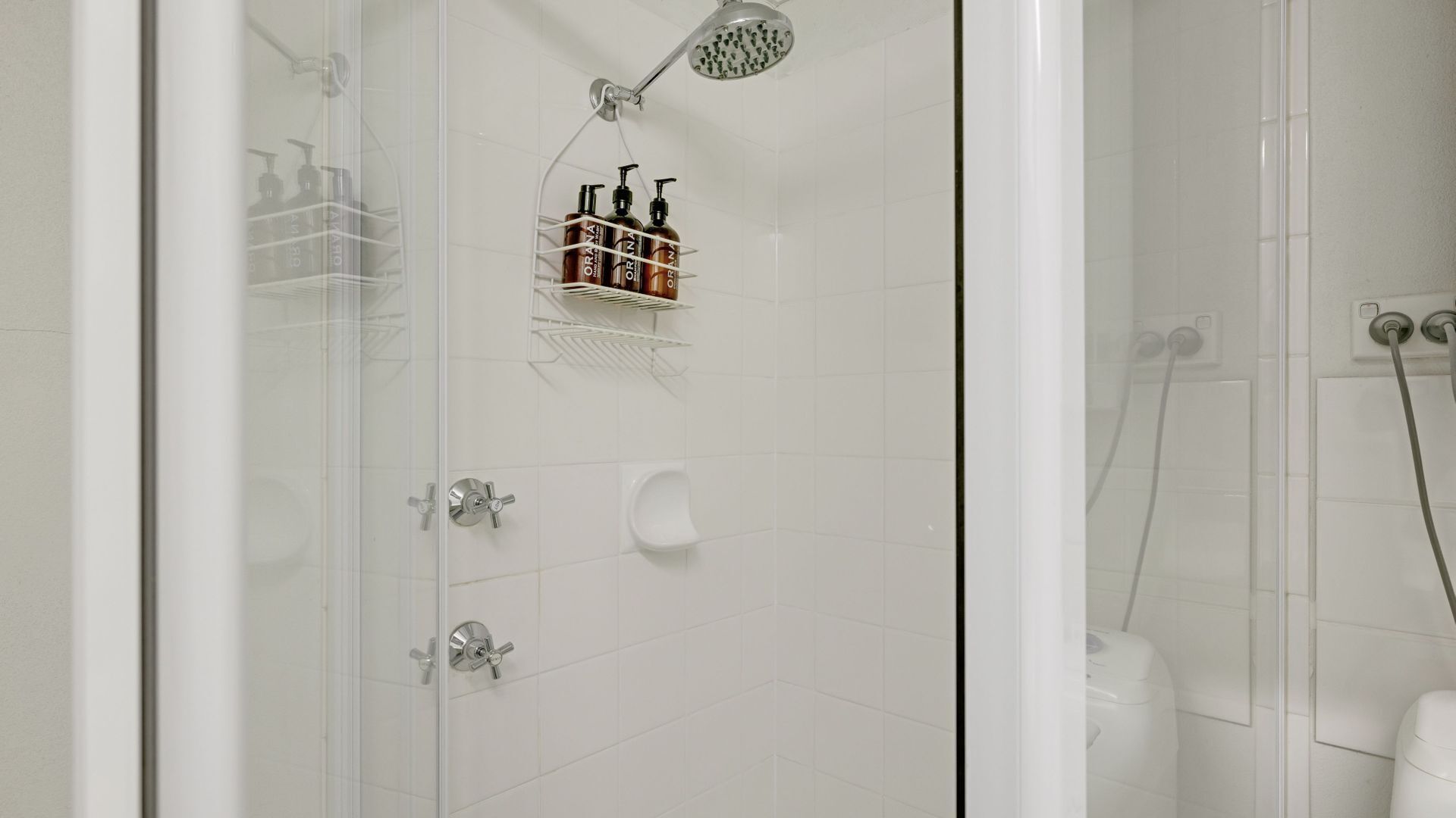 Un baño moderno con cabina de ducha de vidrio, ducha de mano y un estante con artículos de aseo.