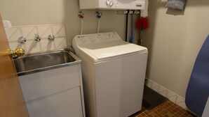 Een kleine wasruimte met een wasmachine en een roestvrijstalen spoelbak.