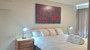 Een hotelkamer met een groot bed, twee nachtkastjes met lampen, een schilderij aan de muur en een raam met gordijnen.
