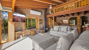 Uma sala de estar acolhedora com lareira, um sofá, uma televisão e uma escada que leva a um andar superior.