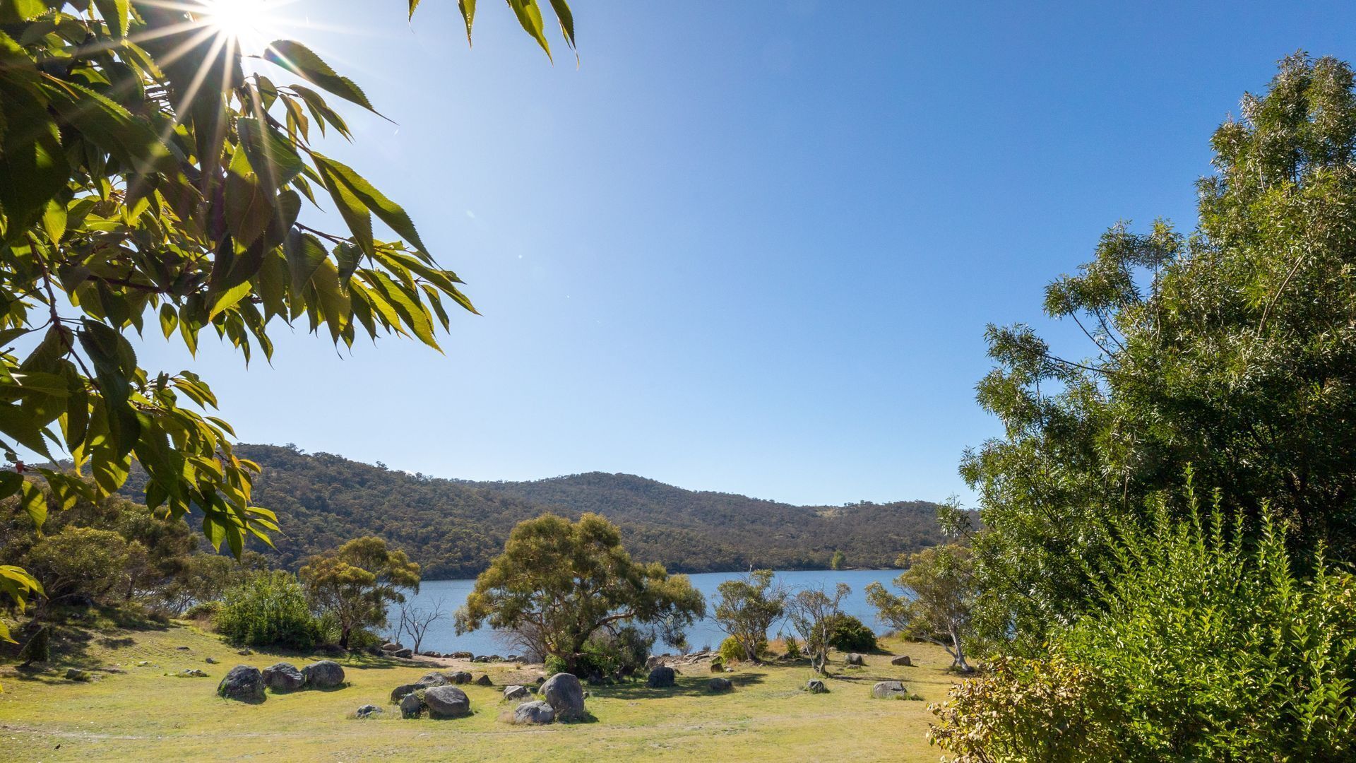 A natural landscape with a lake, trees, and hills in the background.