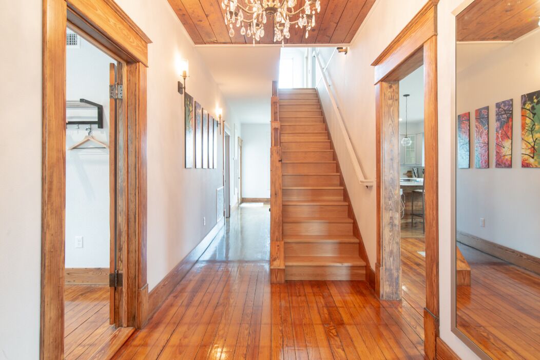 A wooden staircase leading to a second floor, flanked by wooden doors and walls, with a chandelier above.