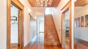 Una escalera de madera conduce a un segundo piso, flanqueada por puertas y paredes de madera, con un candelabro colgando arriba.