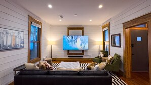 Una sala de estar moderna con un televisor de pantalla plana grande, un sofá de cuero negro y dos sillones.