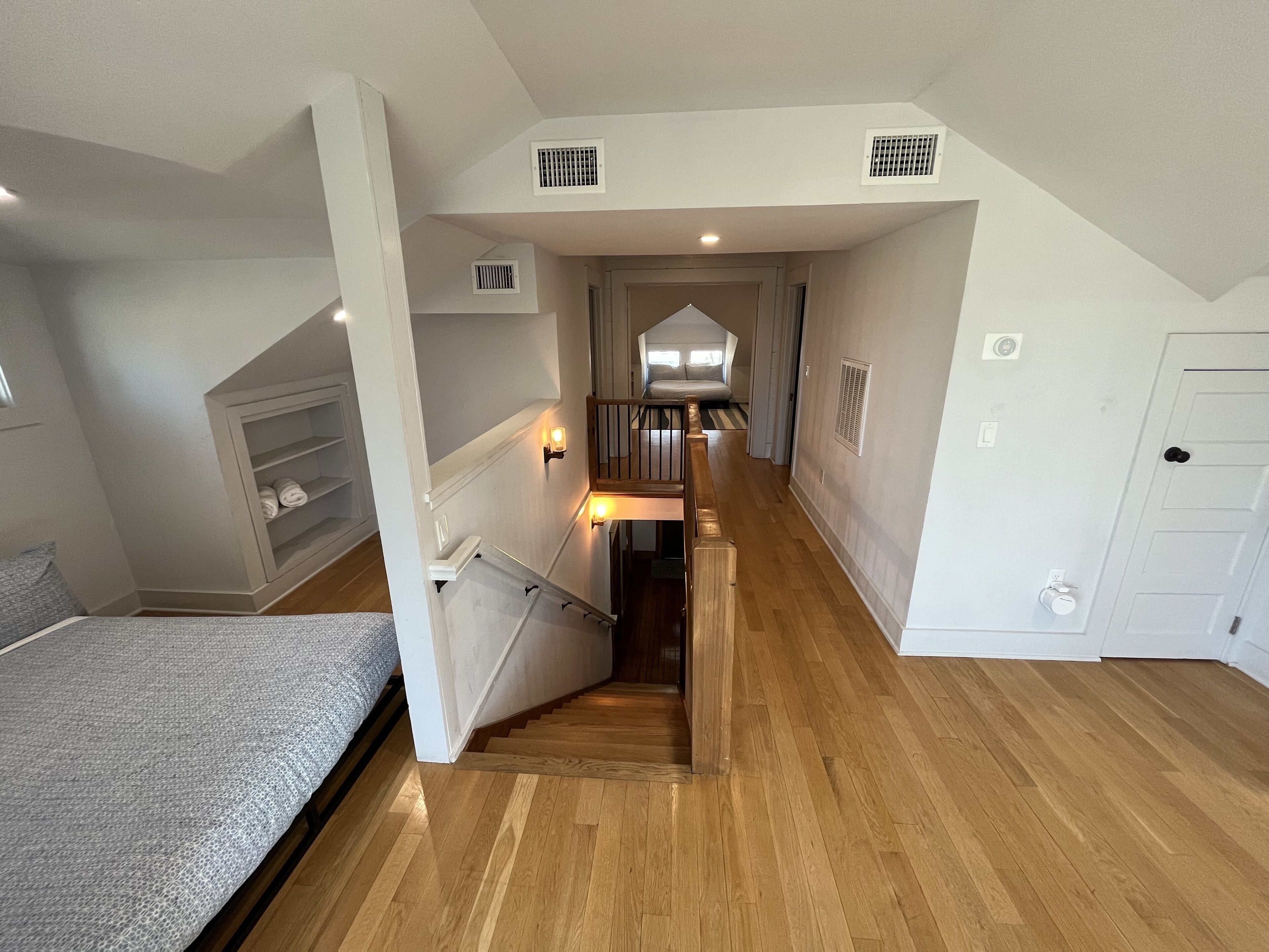A bedroom with a bed, a wooden staircase, and a hallway leading to a bathroom.