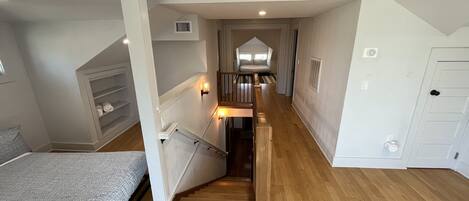 A bedroom with a bed, a wooden staircase, and a hallway leading to a bathroom.
