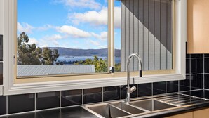 Une cuisine dotée d’une grande fenêtre, d’un évier en acier inoxydable et offrant une vue sur un lac et des collines.