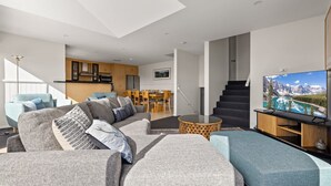 Un salon moderne avec un canapé d’angle, un téléviseur à écran plat et un coin repas doté de meubles en bois.