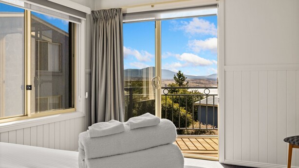 Une chambre d’hôtel avec une grande fenêtre, une vue sur la campagne et une serviette blanche soigneusement pliée posée sur le lit.