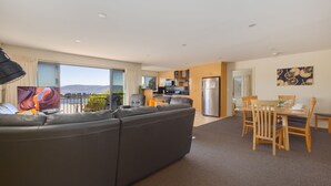 A modern living room with a large sectional sofa, a dining area with wooden furniture, and a kitchen with stainless steel appliances.