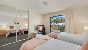 A hotel room with two beds, a TV, a large window with curtains, and a mirror.