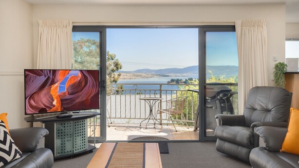 A living room with a TV, two leather sofas, a coffee table, and a balcony with a scenic view.