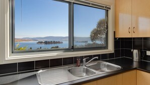 A kitchen with a large window overlooking a lake and distant hills.