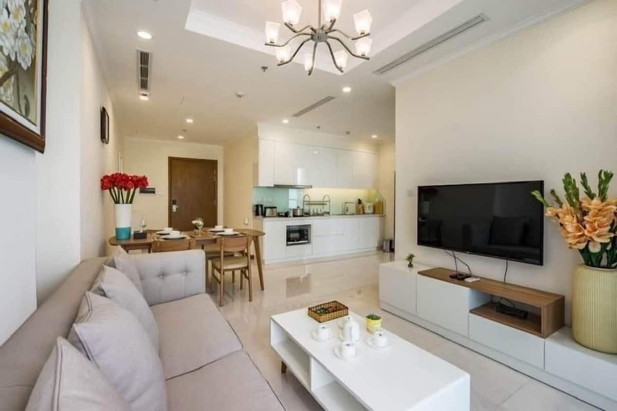Una sala de estar moderna con sofá, mesa de centro, televisor y una cocina al fondo.