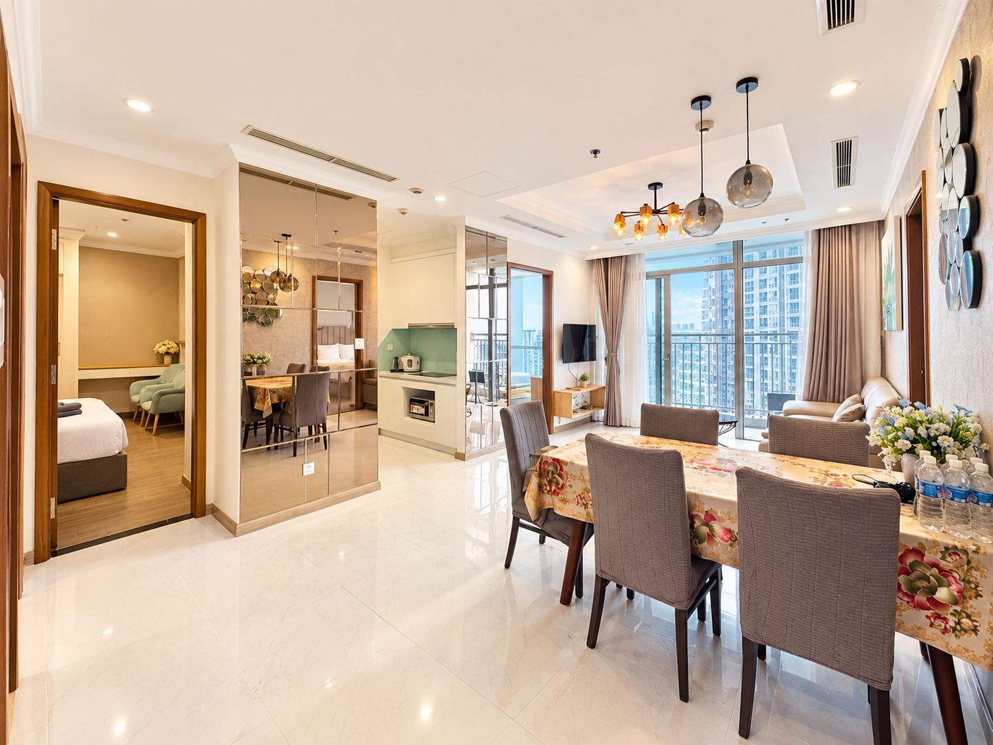 A modern hotel room with a dining area, a kitchen, and a balcony with a city view.