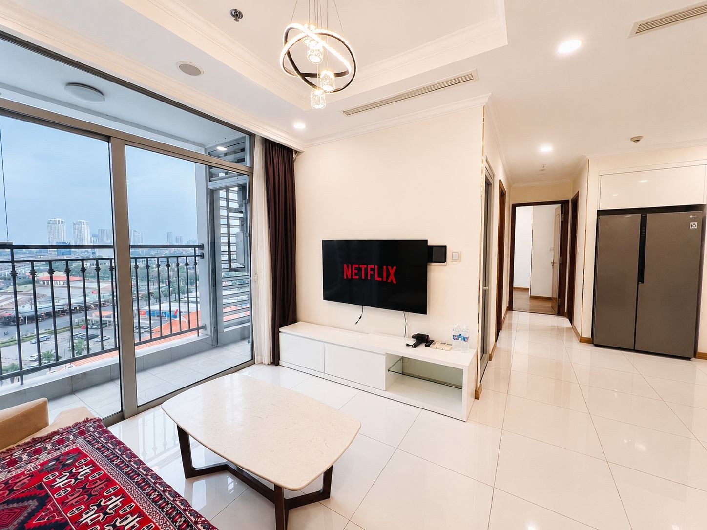 Een moderne woonkamer met een grote televisie, een eettafel en een balkon met uitzicht over de stad.