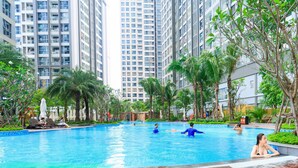 A swimming pool surrounded by tall residential buildings, palm trees, and lounge chairs. - Vinhomes Luxstay Apartment (Ho Chi Minh City)