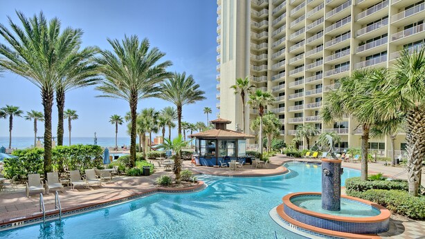 A pool area with palm trees, lounge chairs, and a tall building in the background. - Penthouse@Shores Of Panama 🏖Million Dollar View! (Panama City Beach)