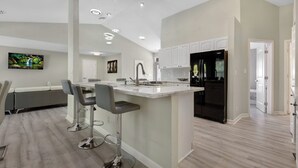 A modern kitchen with white cabinets, a black refrigerator, and a bar area with stools. - PARADIZE FOR EQUESTRIAN LOVERS (Wellington)