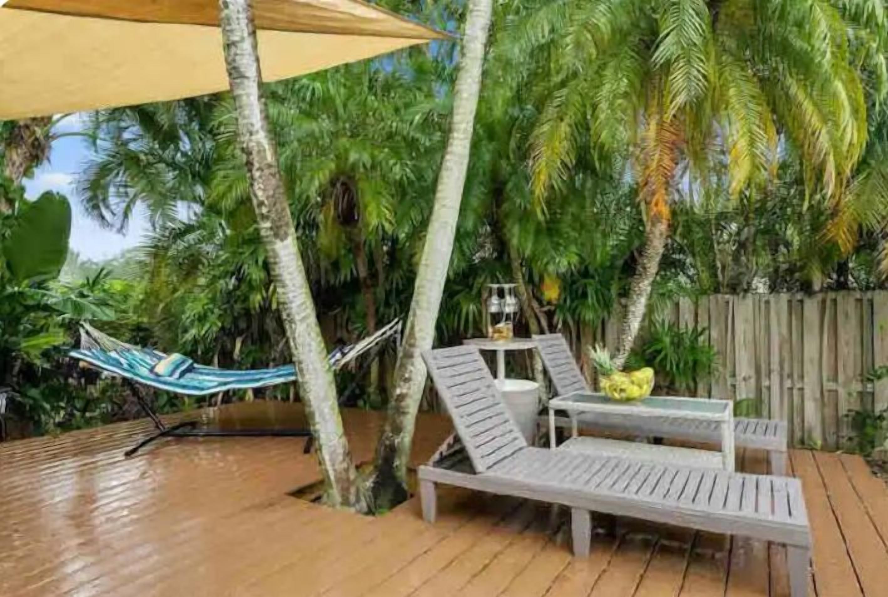 Eine Holzterrasse mit einer Hängematte, zwei Liegestühlen und einem kleinen Tisch mit einem gelben Obst.
