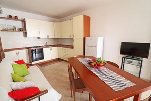 Una cocina compacta con zona de comedor, un sofá con cojines, un televisor sobre un mueble bajo y un frutero sobre la mesa.