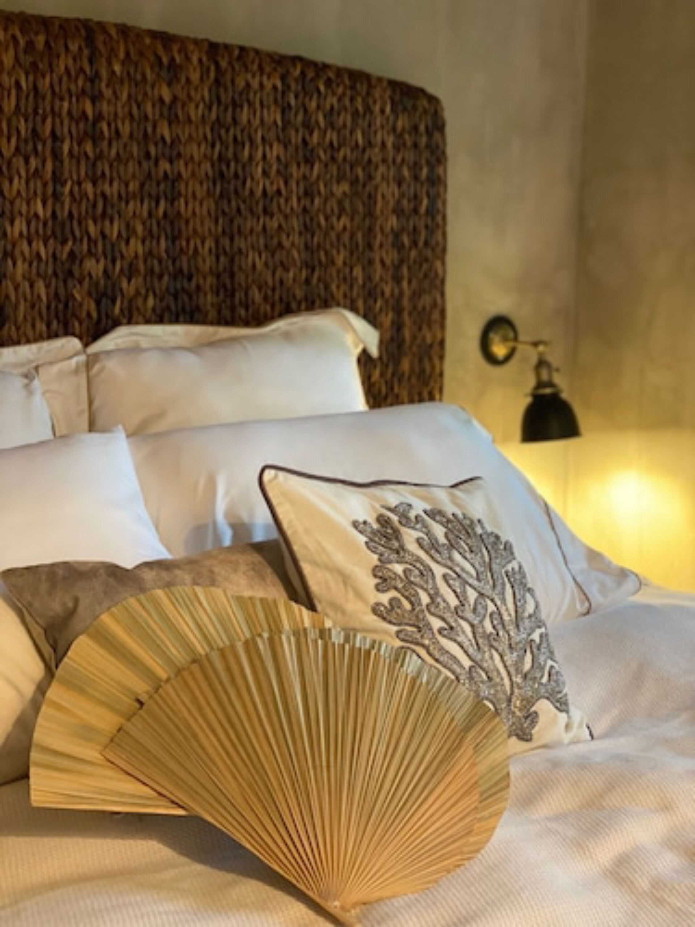 A neatly made bed with white linens and a decorative fan.