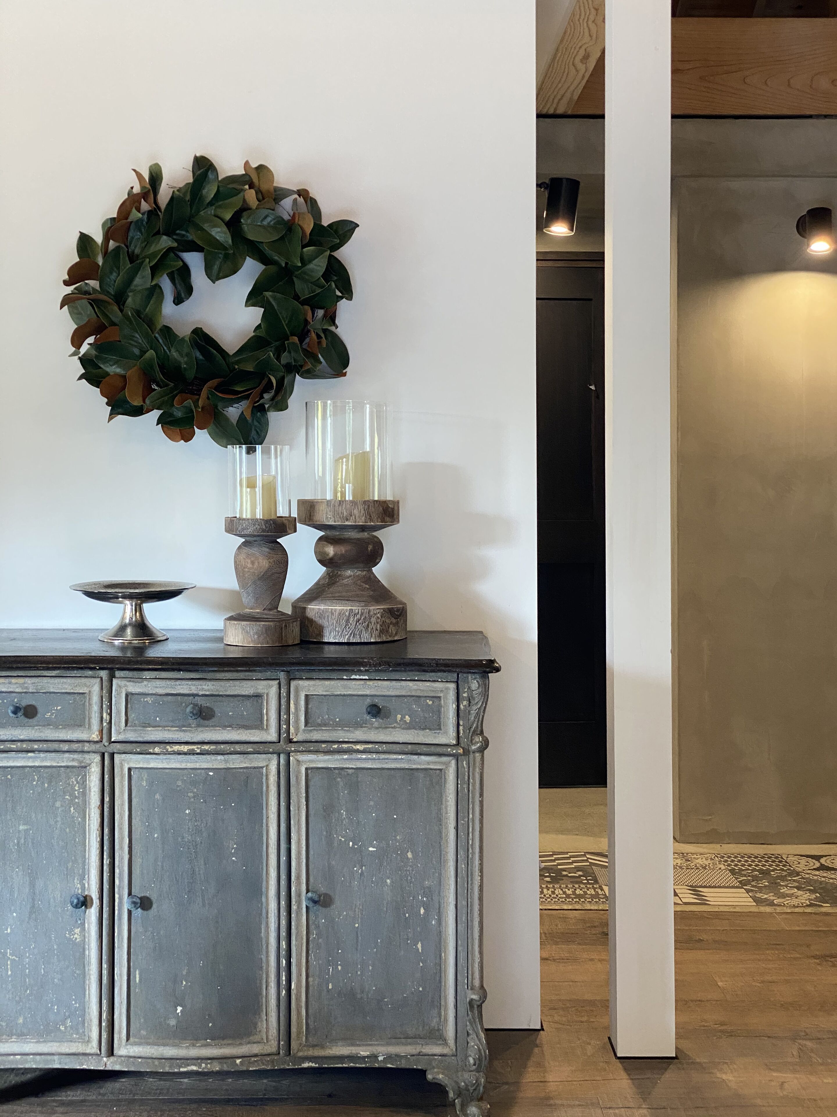 Un aparador de estilo vintage con dos candelabros de vidrio y un arreglo decorativo en la pared de fondo.