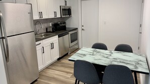 Una cocina compacta con armarios blancos, electrodomésticos de acero inoxidable, una encimera de mármol y dos sillas grises.