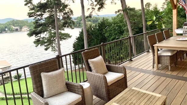 A wooden deck with wicker furniture, overlooking a lake with trees and houses in the background. - Hamilton Happy Place (million dollar view) - Lake Retreat (Hot Springs)
