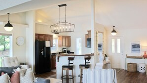 A spacious living area with a grey couch, a coffee table, and a kitchen area with wooden cabinets and a black refrigerator. - Hamilton Happy Place (million dollar view) - Lake Retreat (Hot Springs)