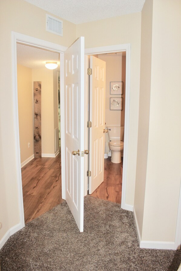 A hallway with a carpeted floor, wooden flooring on the left, and a toilet visible through an open door. - Hamilton Happy Place (million dollar view) - Lake Retreat (Hot Springs)
