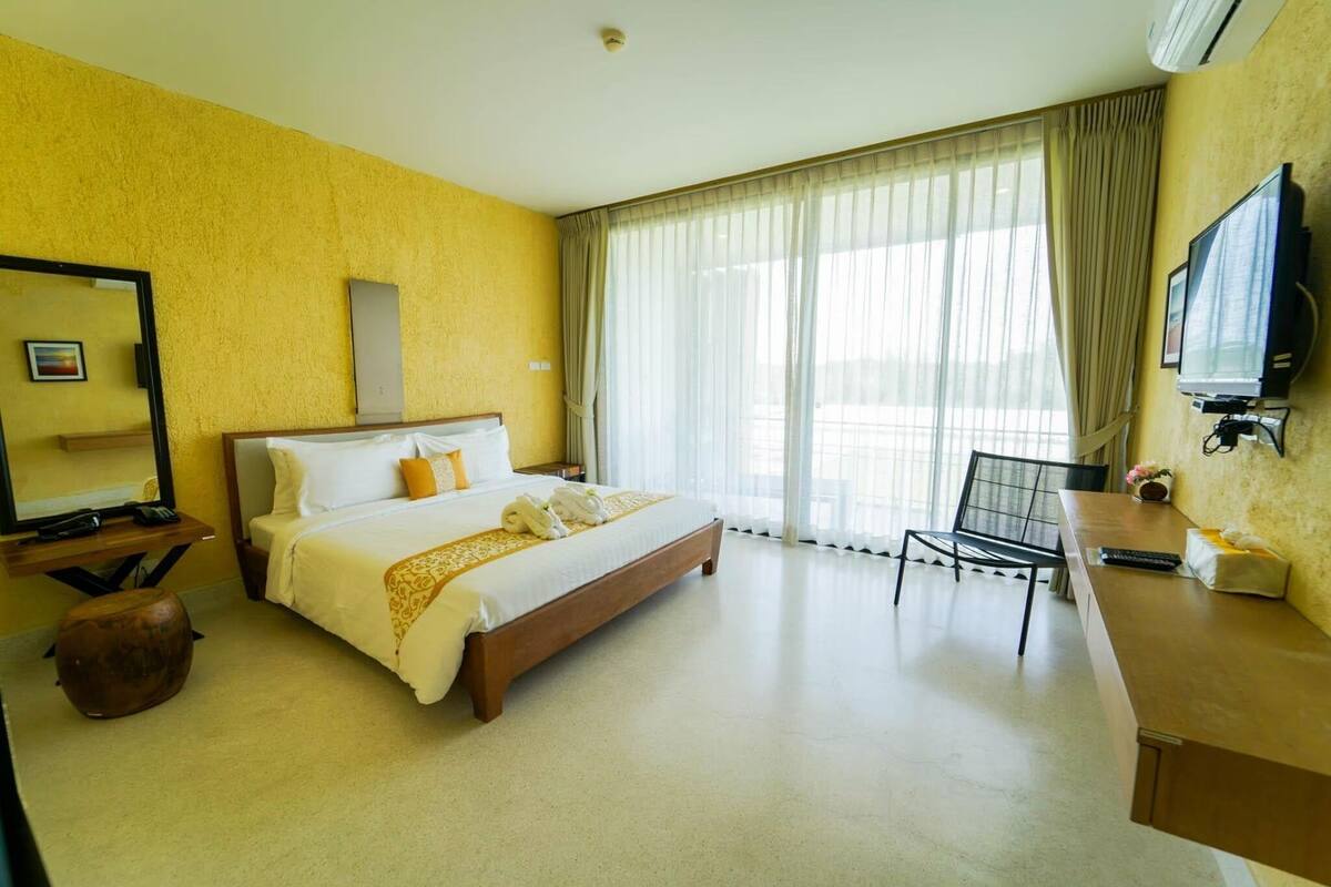 A hotel room with a bed, a desk, a chair, a television, and a large window with curtains.