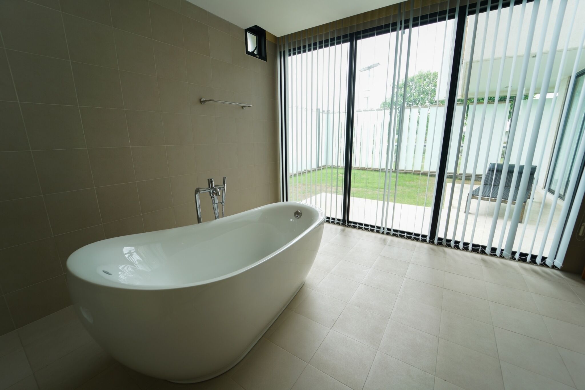 A modern bathroom with a freestanding bathtub, a towel rack, and a large window with blinds.