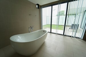 Un baño moderno con una bañera independiente, un perchero y un amplio ventanal con persianas.